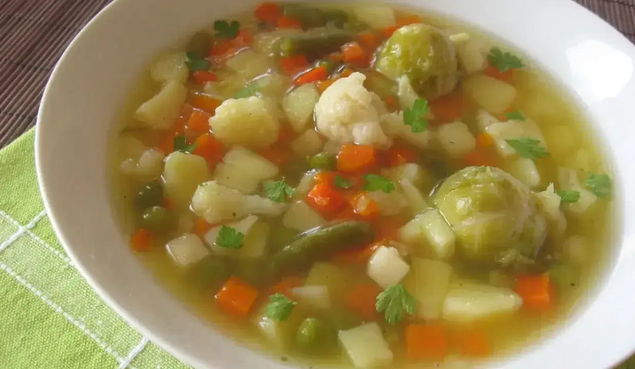 Aromaticzna jarzynowa zupa z ziemniakami, marchewką, kalafiorem i brukselką, udekorowana natką pietruszki.