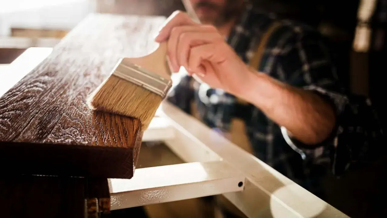 Un artesano aplica barniz a la madera con una brocha, resaltando su veta y dándole un acabado protector.