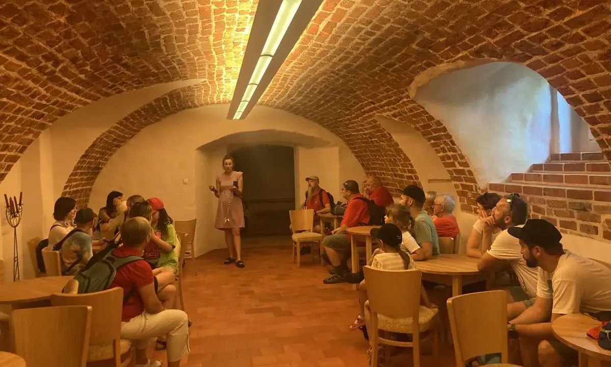 Grupa zwiedza piwnice pałacu w Poddębicach. Przewodniczka opowiada o historii miejsca.