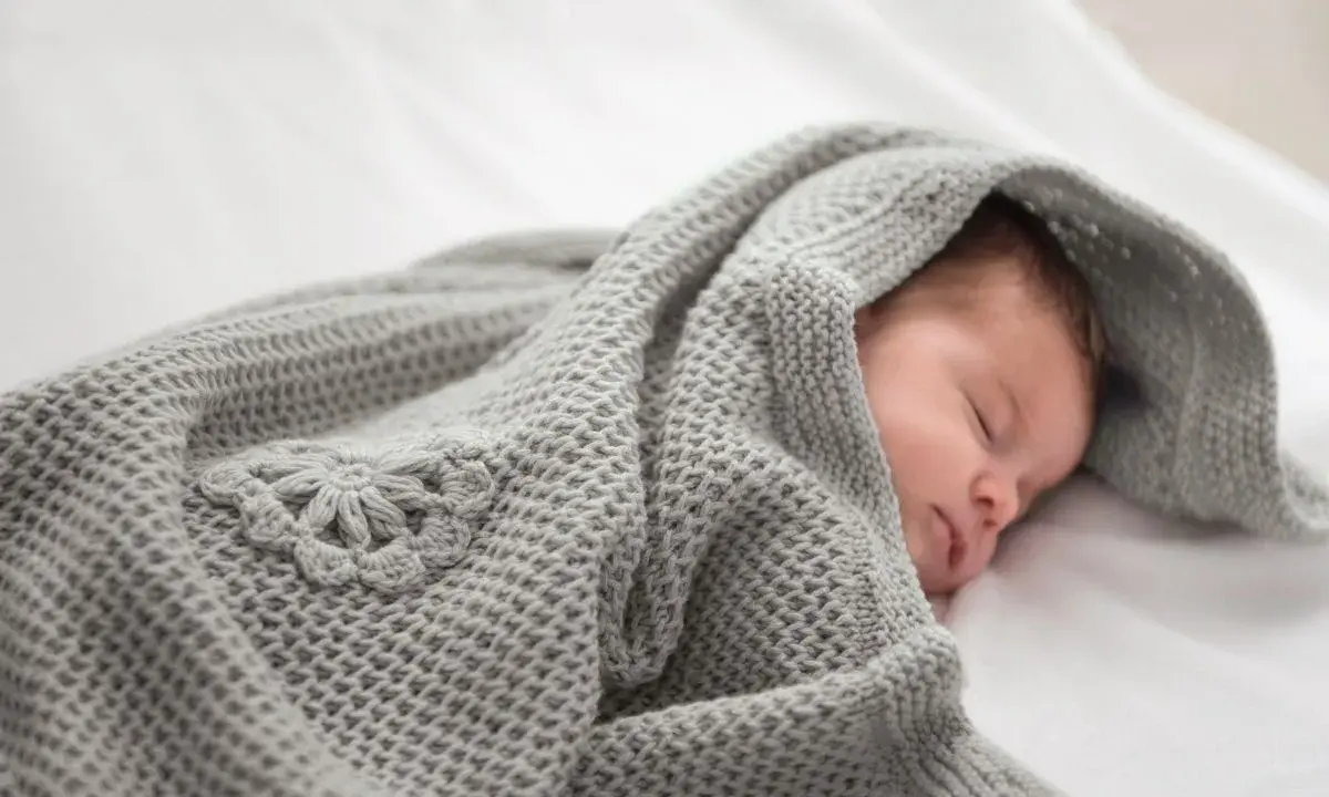 Ein schlafendes Baby, eingewickelt in eine gestrickte Babydecke mit Blumenmuster. Eine Anleitung zum Babydecke stricken wäre hier perfekt.