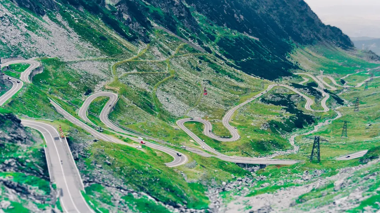 Kręta droga Transalpina wijąca się po zielonych zboczach gór. Widok z lotu ptaka na serpentyny i mosty.