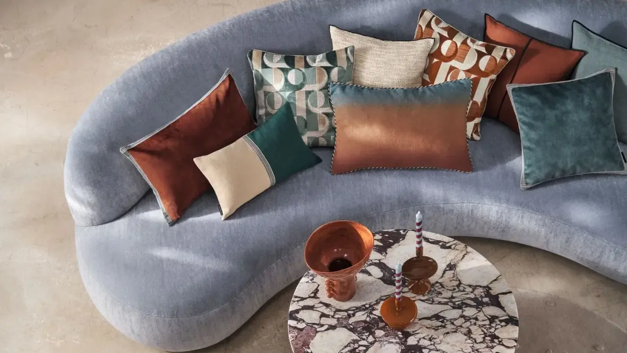 Sofá curvo gris con cojines de terciopelo y estampados geométricos. Un diseño moderno y acogedor.