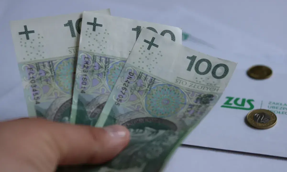 Trzy stuzłotowe banknoty w dłoni, obok dokument ZUS i monety. Czy to 30 krotność zus 2025?