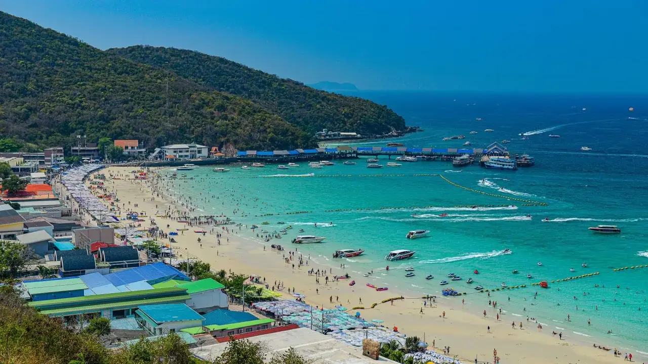 Ein belebter Pattaya Strand mit vielen Menschen, Sonnenschirmen und Booten im türkisfarbenen Meer.
