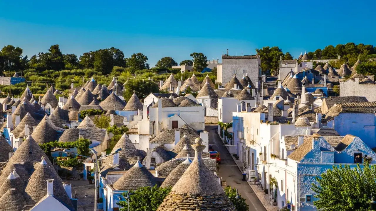 Urokliwe trulli w Alberobello, z ich stożkowymi dachami, tworzą bajkowy krajobraz pod błękitnym niebem.