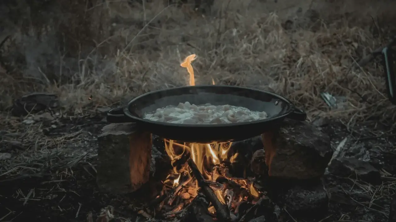 Cuisine en plein air sur un réchaud rocket stove improvisé. Une poêle cuit des aliments sur un feu vif.