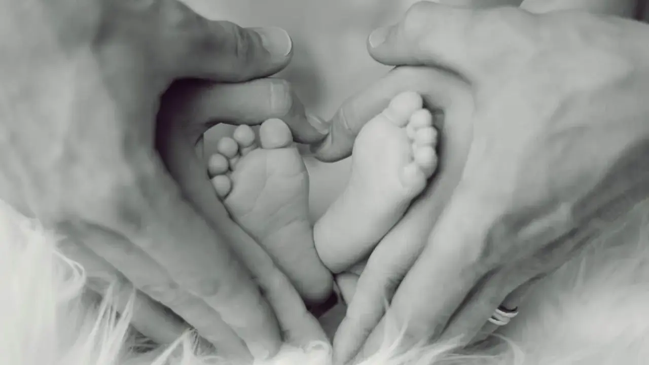 Manos de padre formando un corazón alrededor de los pies de su bebé, un símbolo de apego excesivo al padre y amor incondicional.
