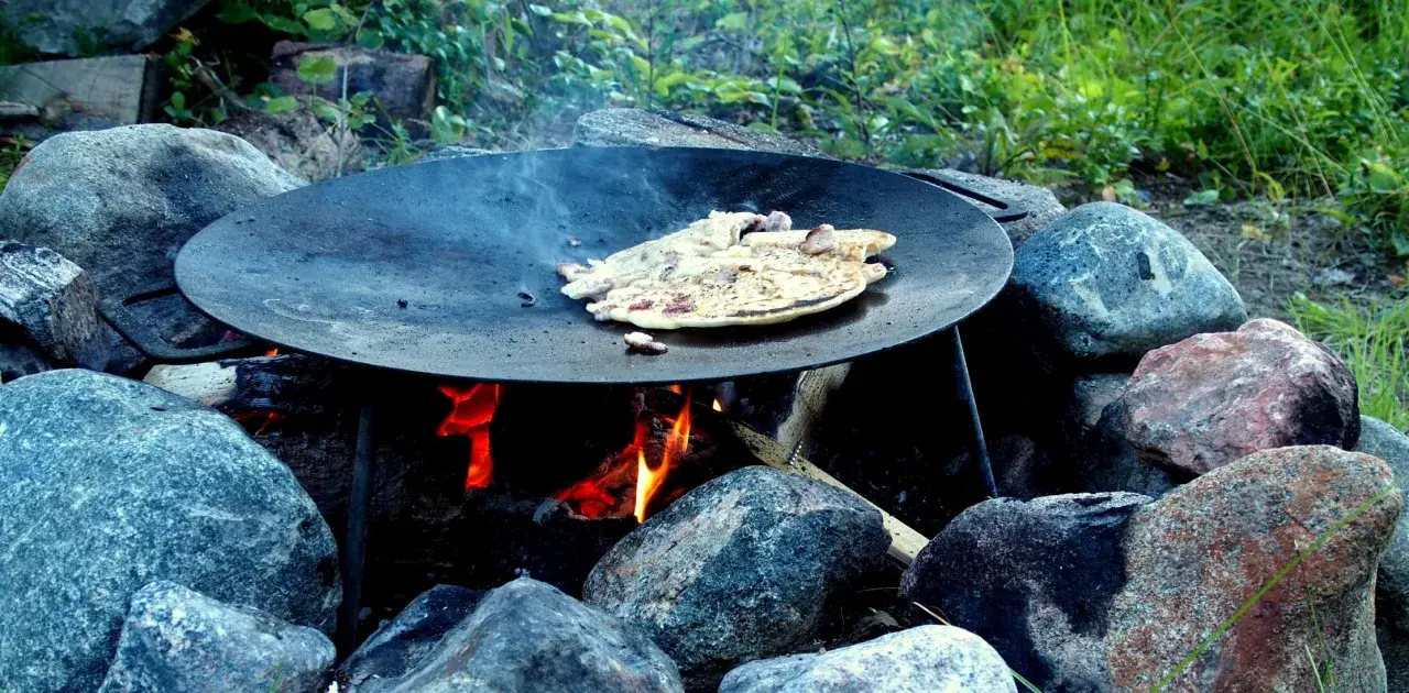 Matlagning över öppen eld på ett muurikka ställning. Pannkakor steks i en stor stekpanna över glödande kol och ved.