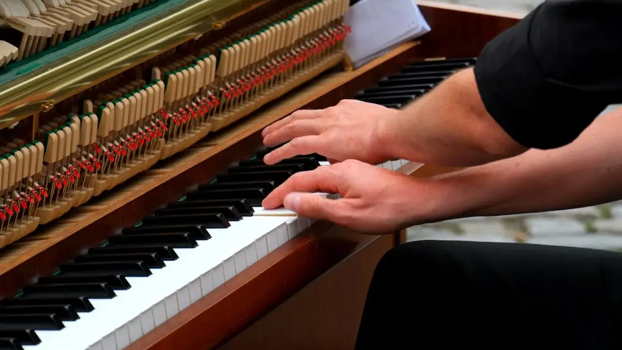 Mains sur le clavier d'un piano, prêt à jouer d'un instrument. Les marteaux et les cordes sont visibles.