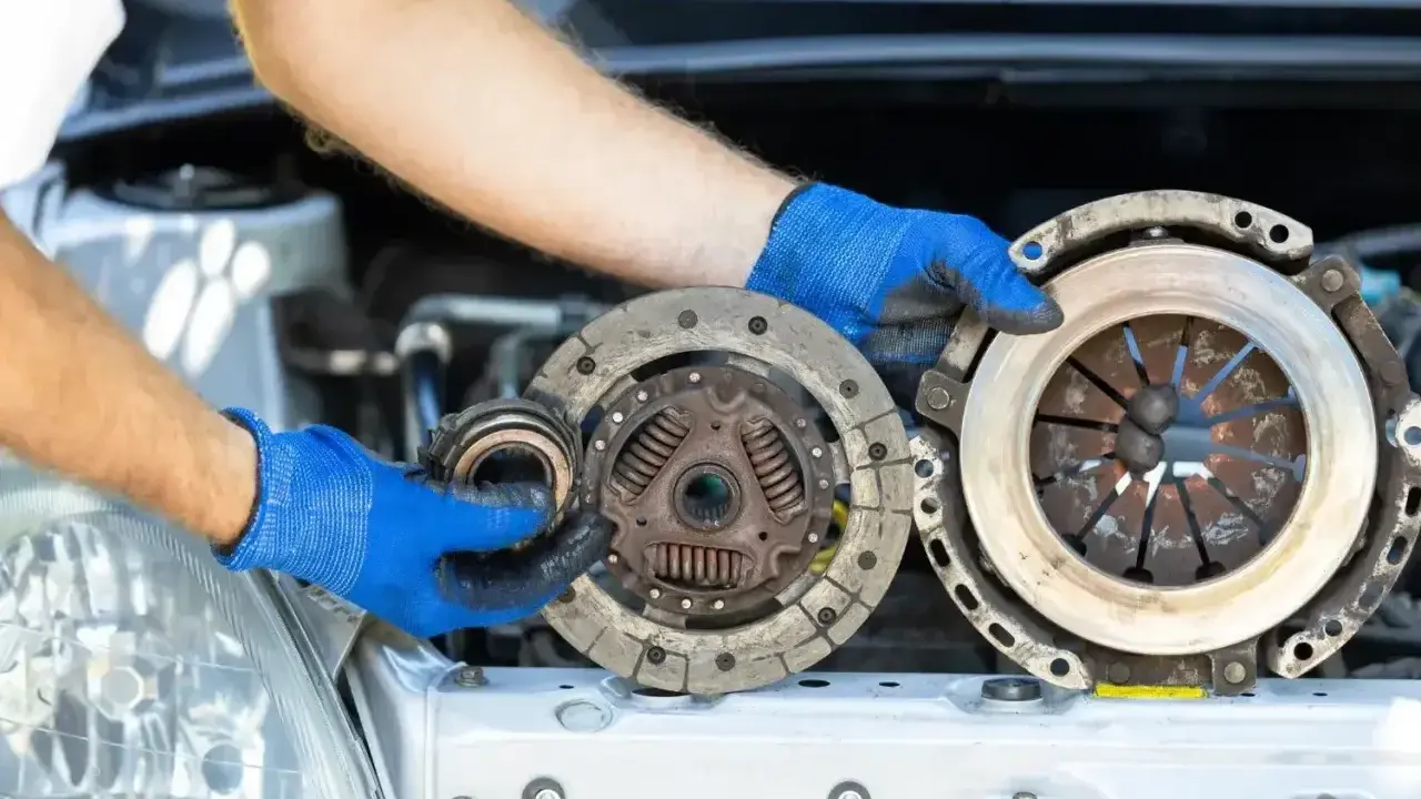 Mechanik w niebieskich rękawiczkach trzyma części samochodowe. Wygląda na to, że właśnie wymienia ślizgające się sprzęgło.