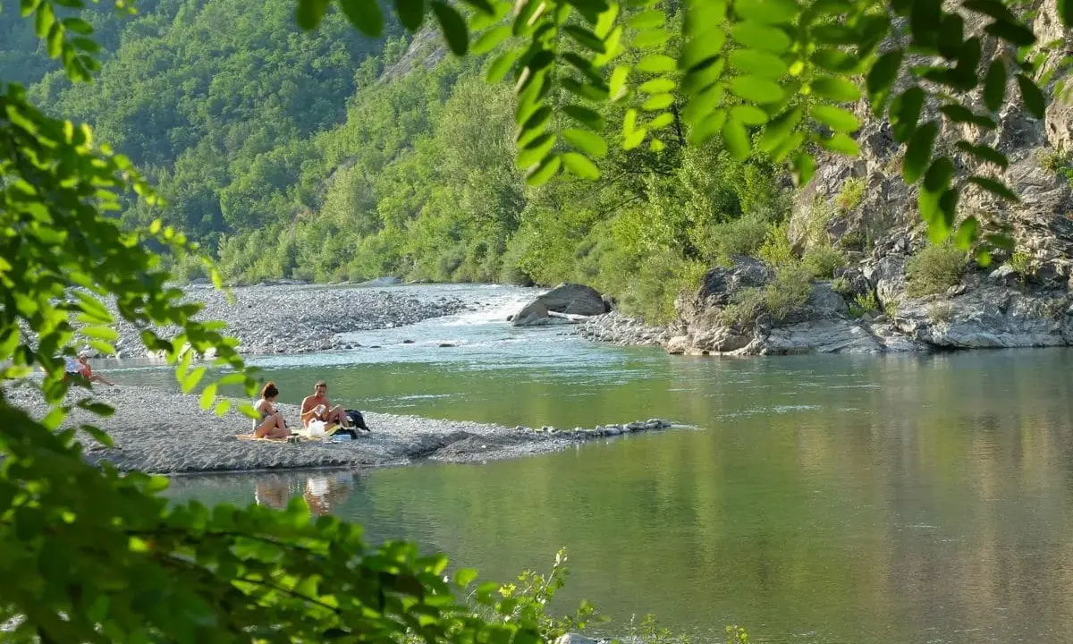 Un **lago vicino Milano con spiaggia** dove coppie si rilassano tra rocce e vegetazione lussureggiante.