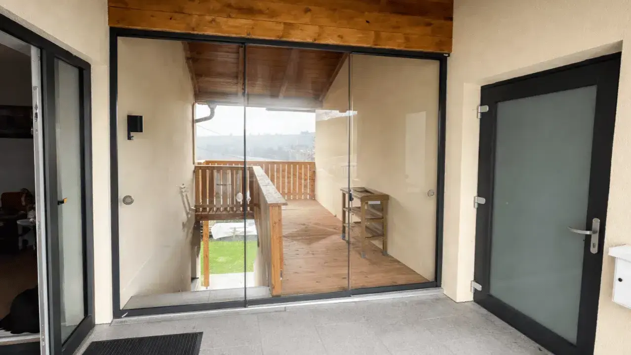 Moderner, verglaster Windfang aus Aluminium mit Holzbalken und Blick auf eine Holzterrasse.