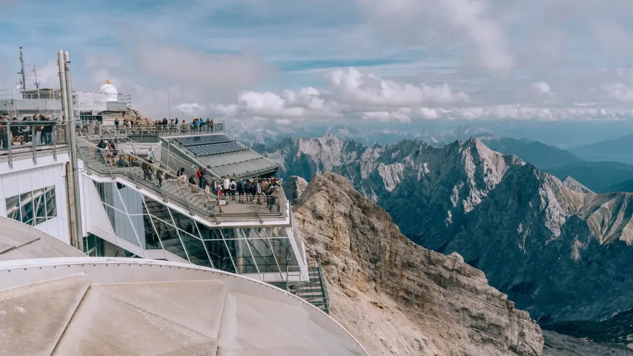 Tłum turystów na tarasie widokowym najwyższego szczytu Niemiec, Zugspitze, podziwia alpejskie krajobrazy.