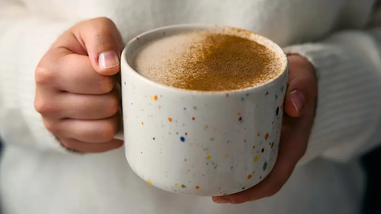 Ciepły napój w kolorowym kubku, posypany cynamonem. Czy to chai latte? Idealny na chłodne dni.