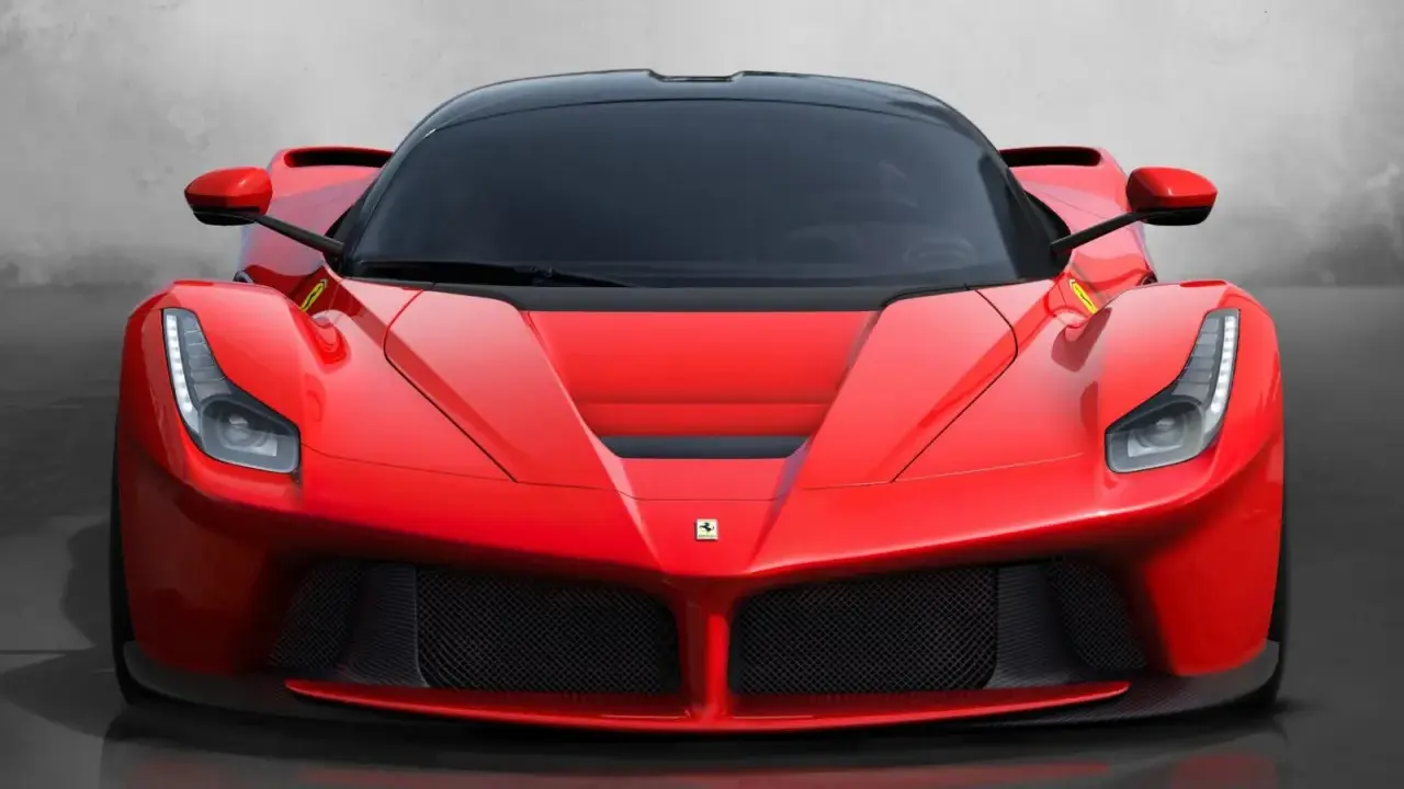 Przód czerwonego LaFerrari z czarnym dachem i przyciemnianymi szybami, błyszczący na tle szarej ściany.