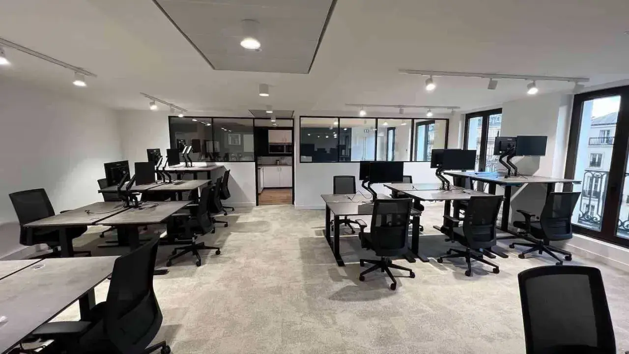 Bureau moderne avec postes de travail réglables en hauteur, écrans d'ordinateur et chaises ergonomiques. L'espace semble propre, mais on pourrait y sentir un air vicié sans fenêtres ouvertes.