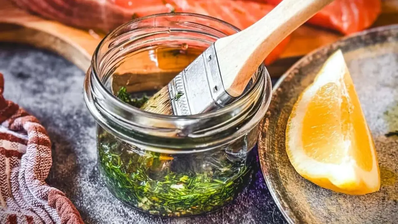 Marinade mit Kräutern und Zitrone bereit, um den Lachs zu verfeinern. Ein Pinsel liegt in der Glasflasche.