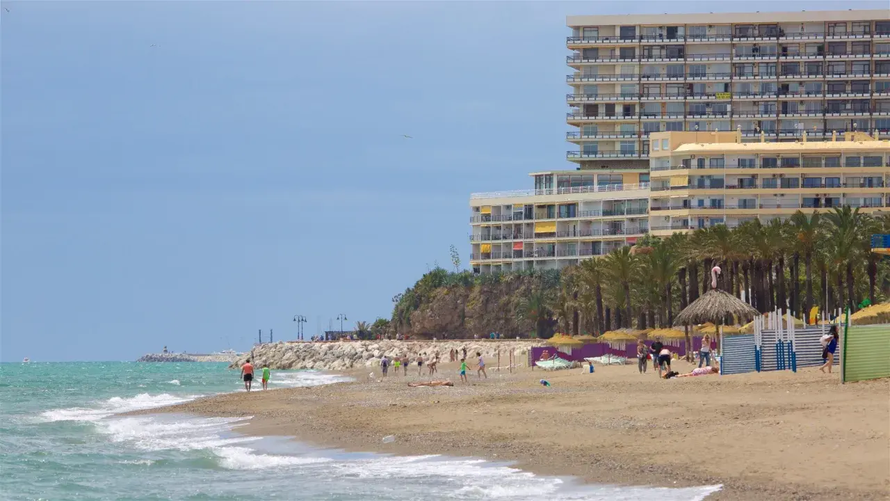 Menschen genießen den sonnigen torremolinos strand mit Palmen und einem großen Hotel im Hintergrund.