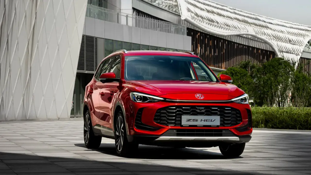 Czerwony MG ZS HEV, nowoczesny SUV hybrydowy, zaparkowany przed futurystycznym budynkiem.