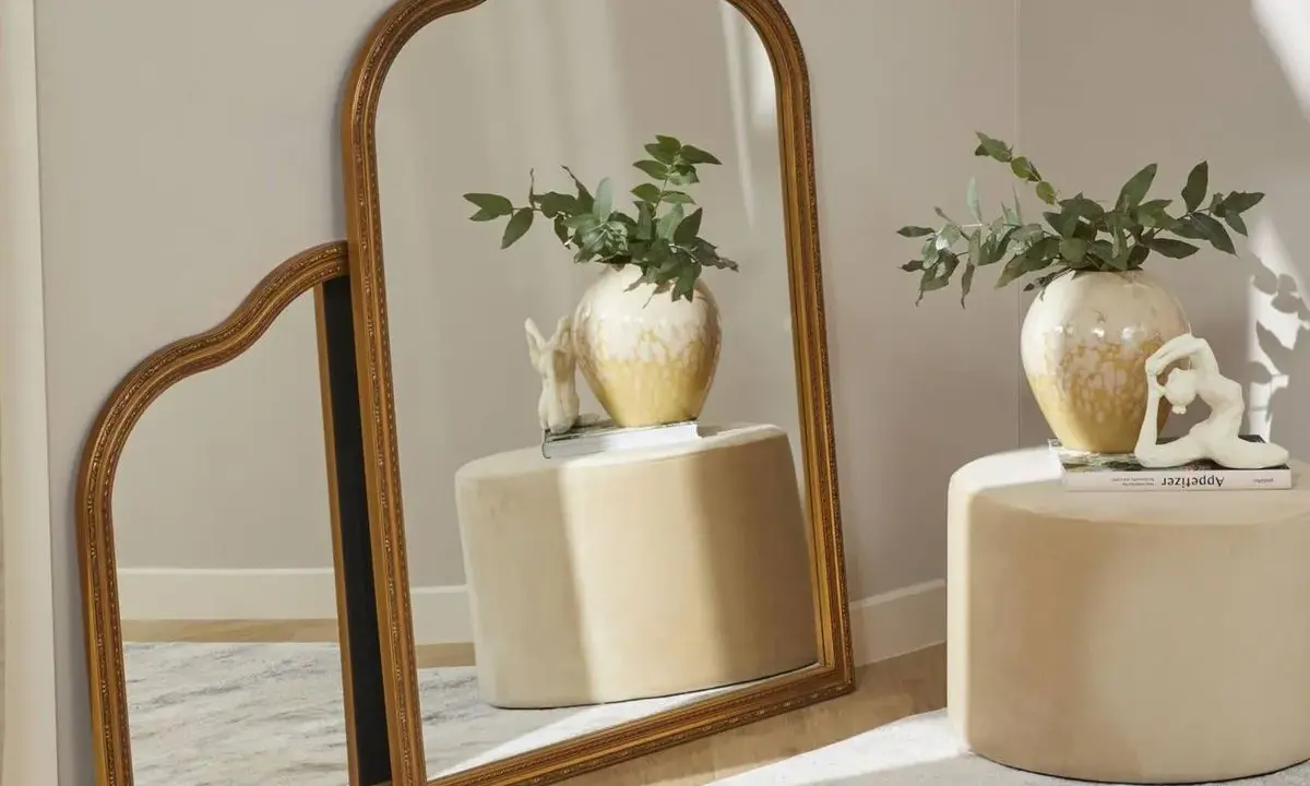Dos espejos dorados, uno grande y otro pequeño, apoyados en la pared. Ideas para como colocar espejos pequeños en la pared.