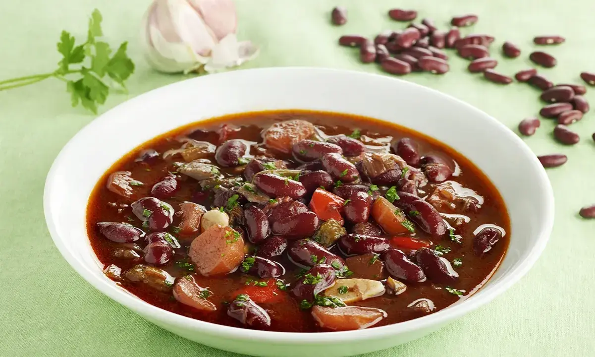 Un plato humeante de judías pintas con trozos de carne y verduras, decorado con perejil fresco.