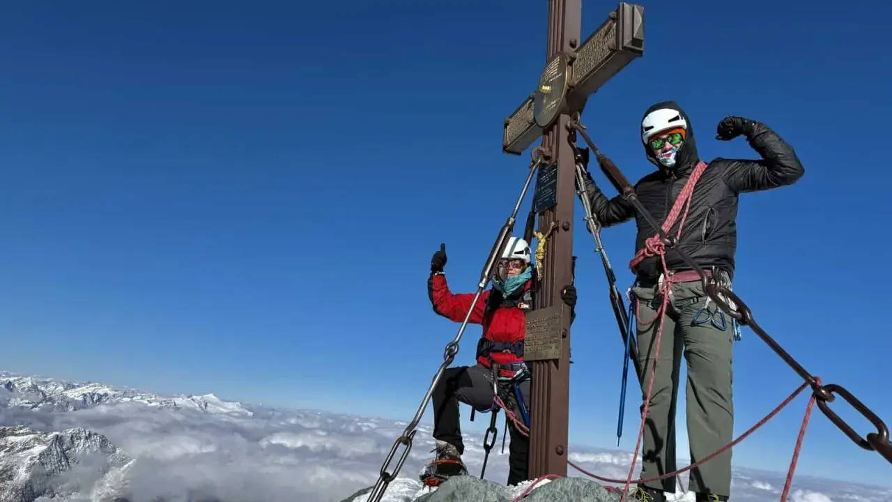 Dwóch alpinistów na szczycie najwyższego szczytu w Austrii. Widok na góry i chmury poniżej.