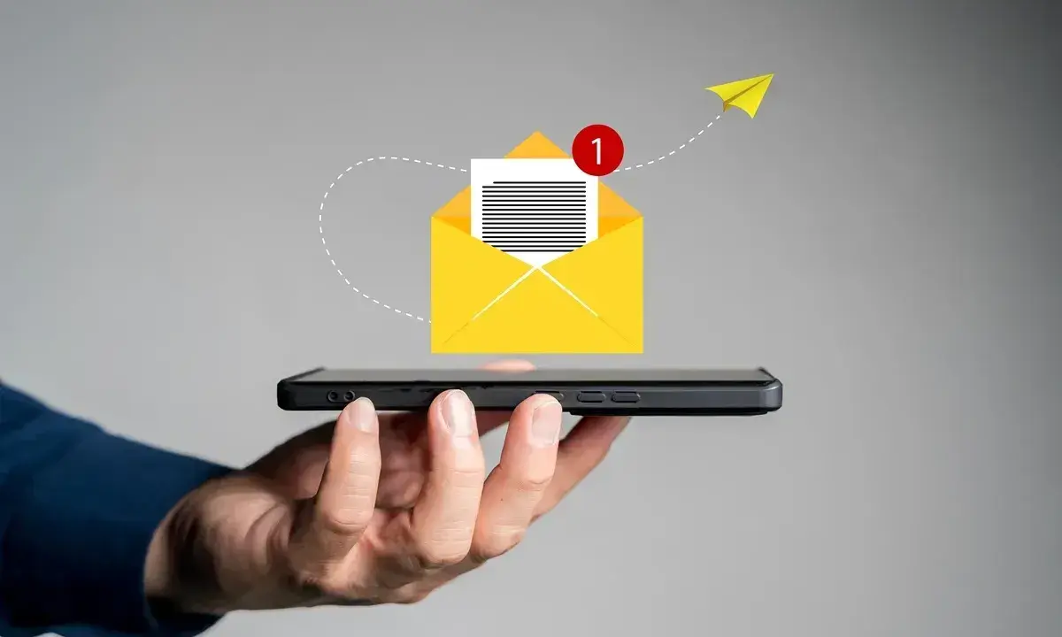 Dłoń trzyma smartfon, z którego wylatuje żółta koperta z powiadomieniem. Jak napisać SMSa o urlop na żądanie?