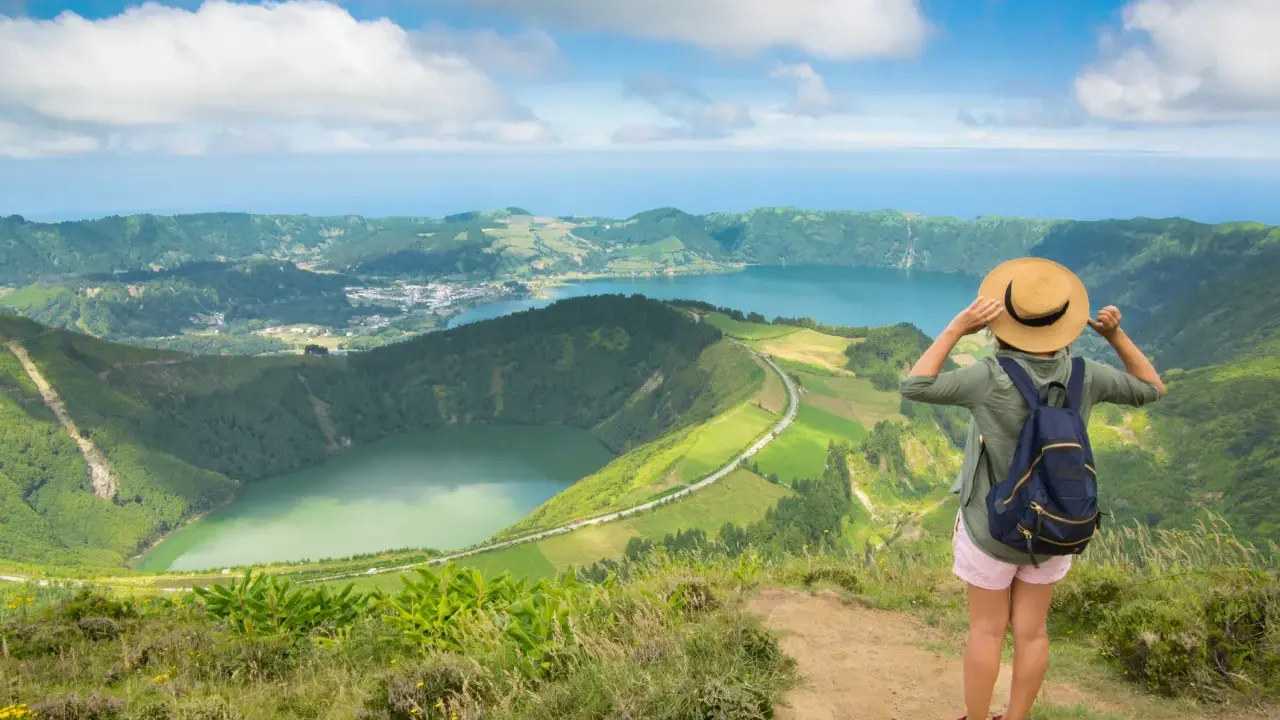Frau mit Hut und Rucksack genießt den Ausblick auf die Azoren. Perfekte azoren beste reisezeit für dieses Panorama.
