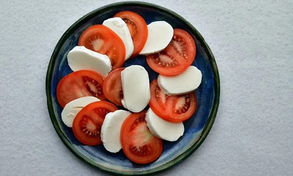 Plasterka pomidorów i mozzarelli ułożone naprzemiennie na niebieskim talerzu.