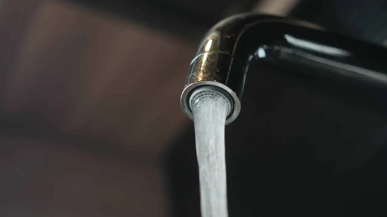 Un robinet chromé verse un jet d'eau. L'image évoque la dureté de l'eau par commune en France, un sujet important pour la vie quotidienne.