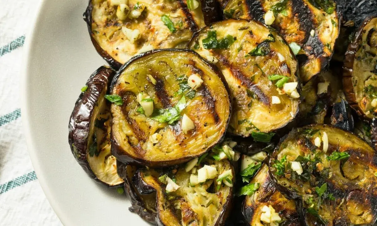 Aubergines grillées en rondelles, garnies d'ail et de persil, sur une assiette.