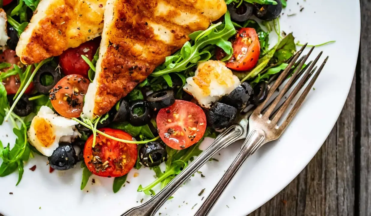 Pyszna sałatka z grillowanym halloumi, pomidorkami koktajlowymi i czarnymi oliwkami, podana z rukolą.