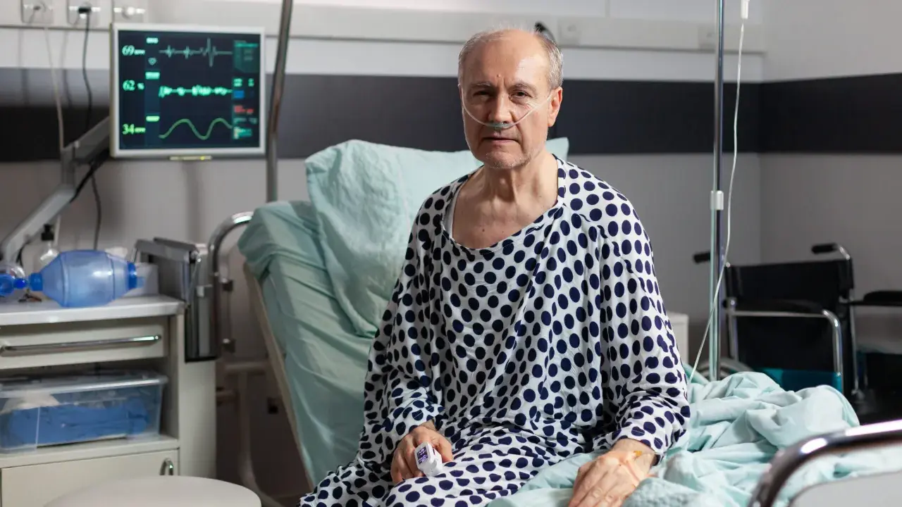 Starszy mężczyzna w szpitalnym łóżku, z tlenem w nosie, walczy z ostrą białaczką szpikową. Monitor pokazuje jego parametry życiowe.
