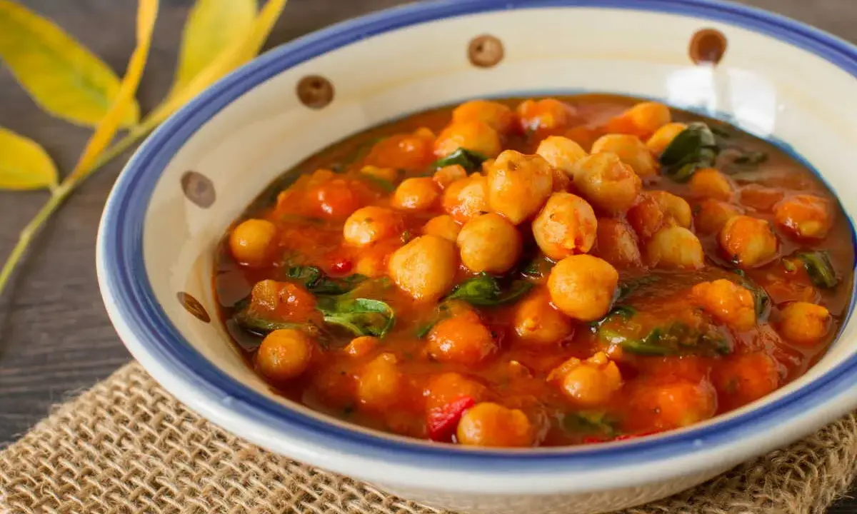 Un savoureux curry de pois chiche, aux couleurs chaudes, servi dans un bol décoré. Une touche de verdure et des feuilles jaunes apportent une note automnale.