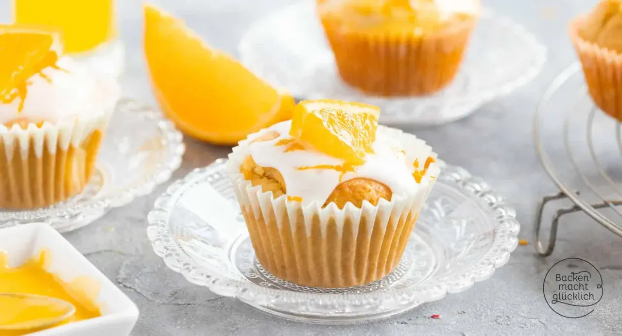Fanta Muffins mit weißer Glasur und Orangenspalten, serviert auf kleinen Glastellern.