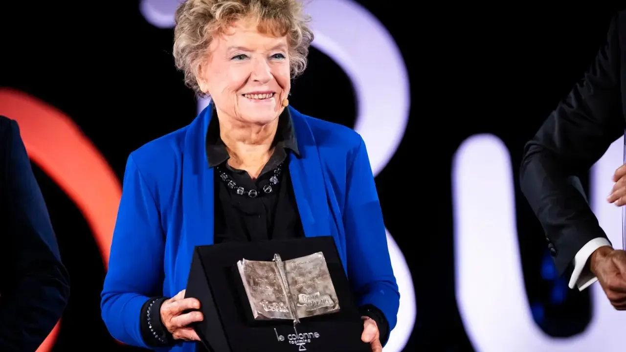 Una donna sorride sul palco, tenendo un premio a forma di libro aperto. Un simbolo di ispirazione per le libere donne.