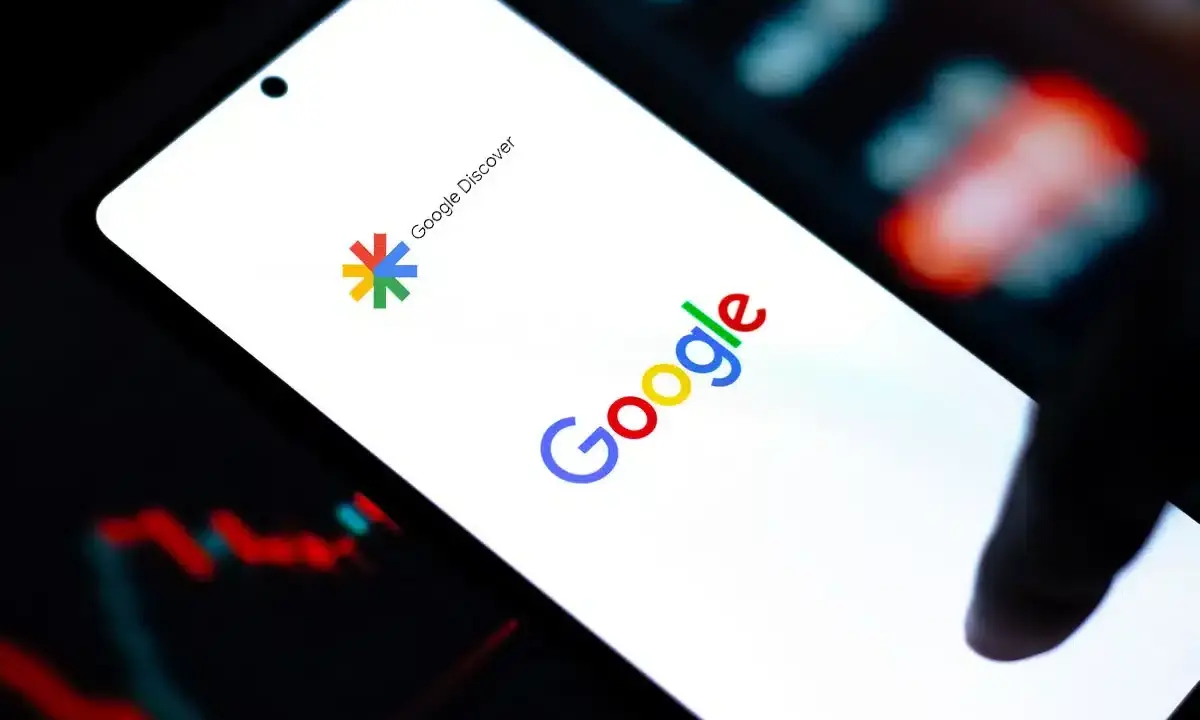 Ekran smartfona z logo Google i napisem Google Discover. W tle wykresy giełdowe.