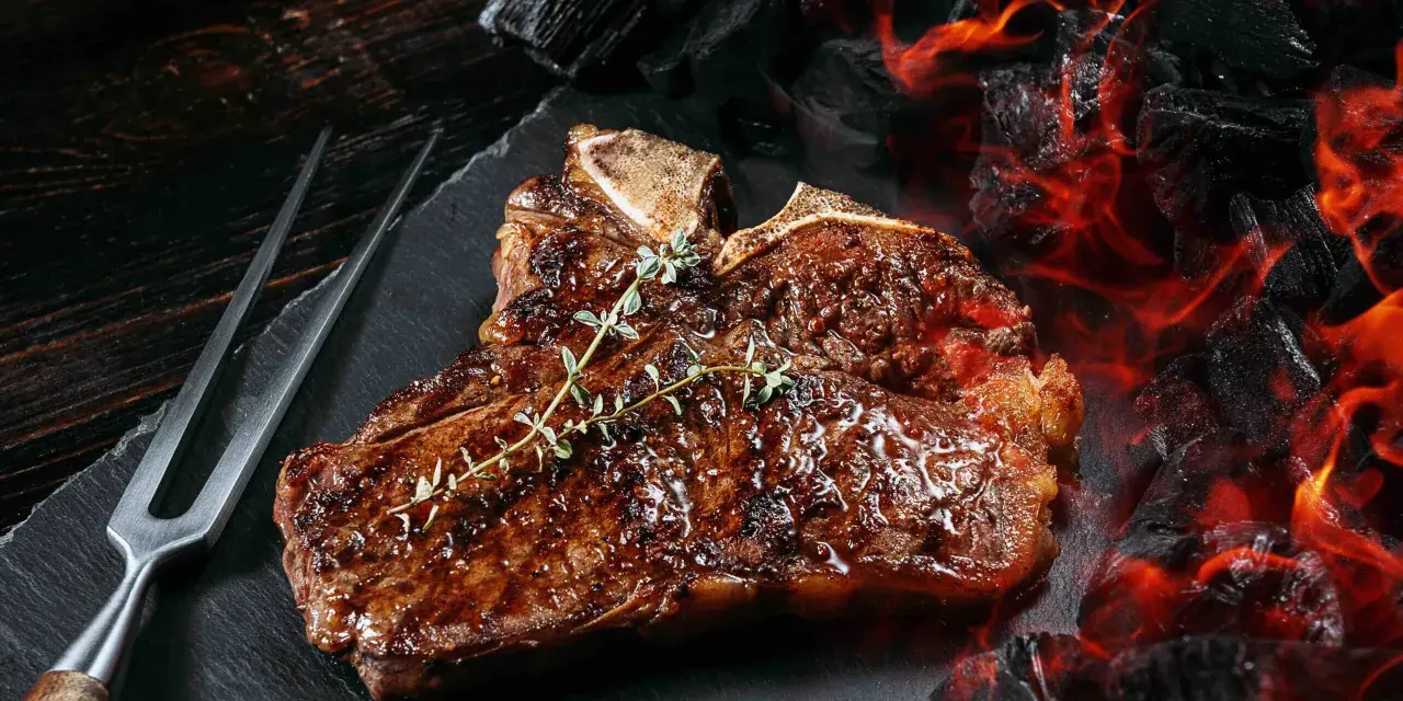 Un jugoso chuleton a la brasa, con romero fresco, listo para ser servido junto a brasas ardientes.