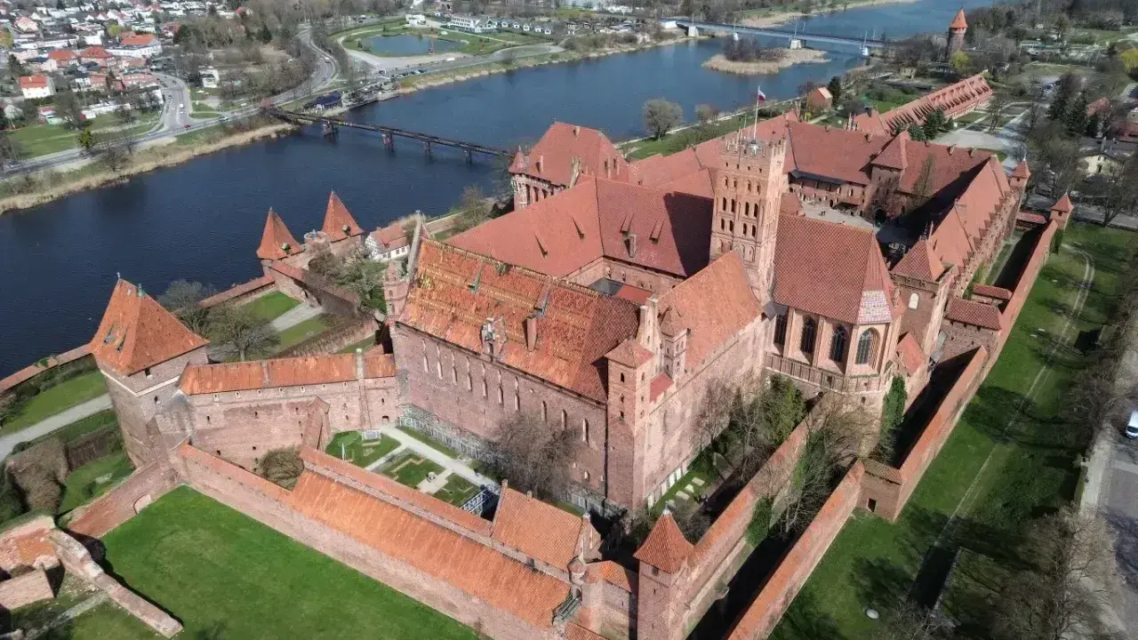 Malbork, największy zamek w Polsce, rozciąga się wzdłuż rzeki Nogat. Potężne ceglane mury i wieże świadczą o jego historycznym znaczeniu.