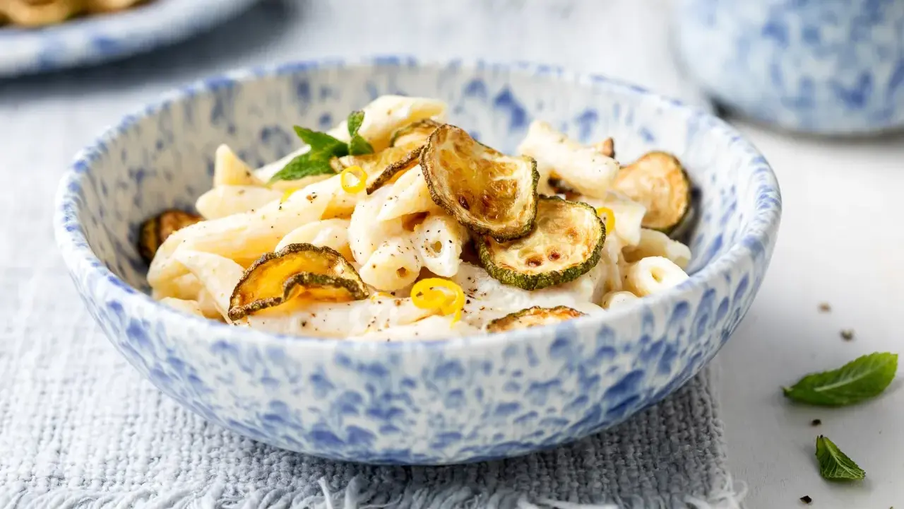 Piatto di pasta cremosa con ricotta e zucchine croccanti, guarnito con scorza di limone e menta.