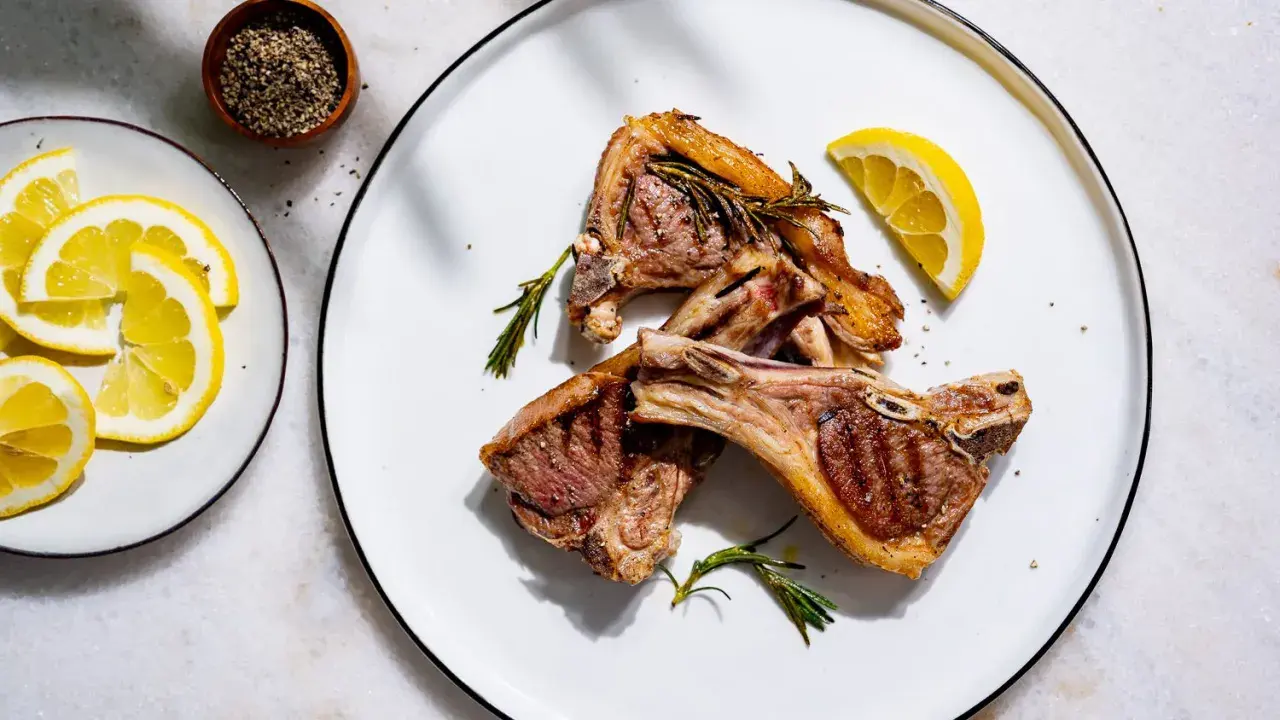 Côtelettes d'agneau grillées, parfumées à la marinade, garnies de romarin frais et de quartiers de citron.