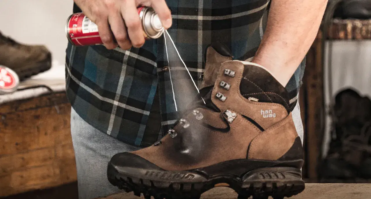 Jak zabezpieczyć nowe buty skórzane? Mężczyzna spryskuje brązowe buty trekkingowe preparatem ochronnym.