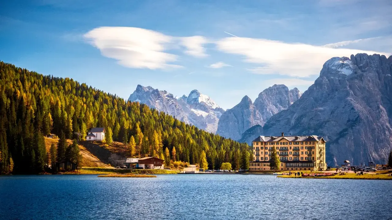 Lago alpino con hotel giallo e boschi autunnali, ideale tra i laghi da visitare in giornata.