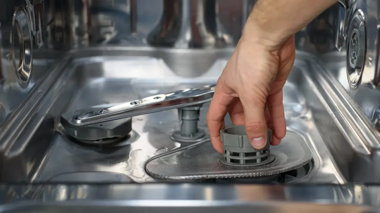 Main d'homme retirant le filtre du lave-vaisselle, une étape avant le nettoyage avec de l'acide citrique.