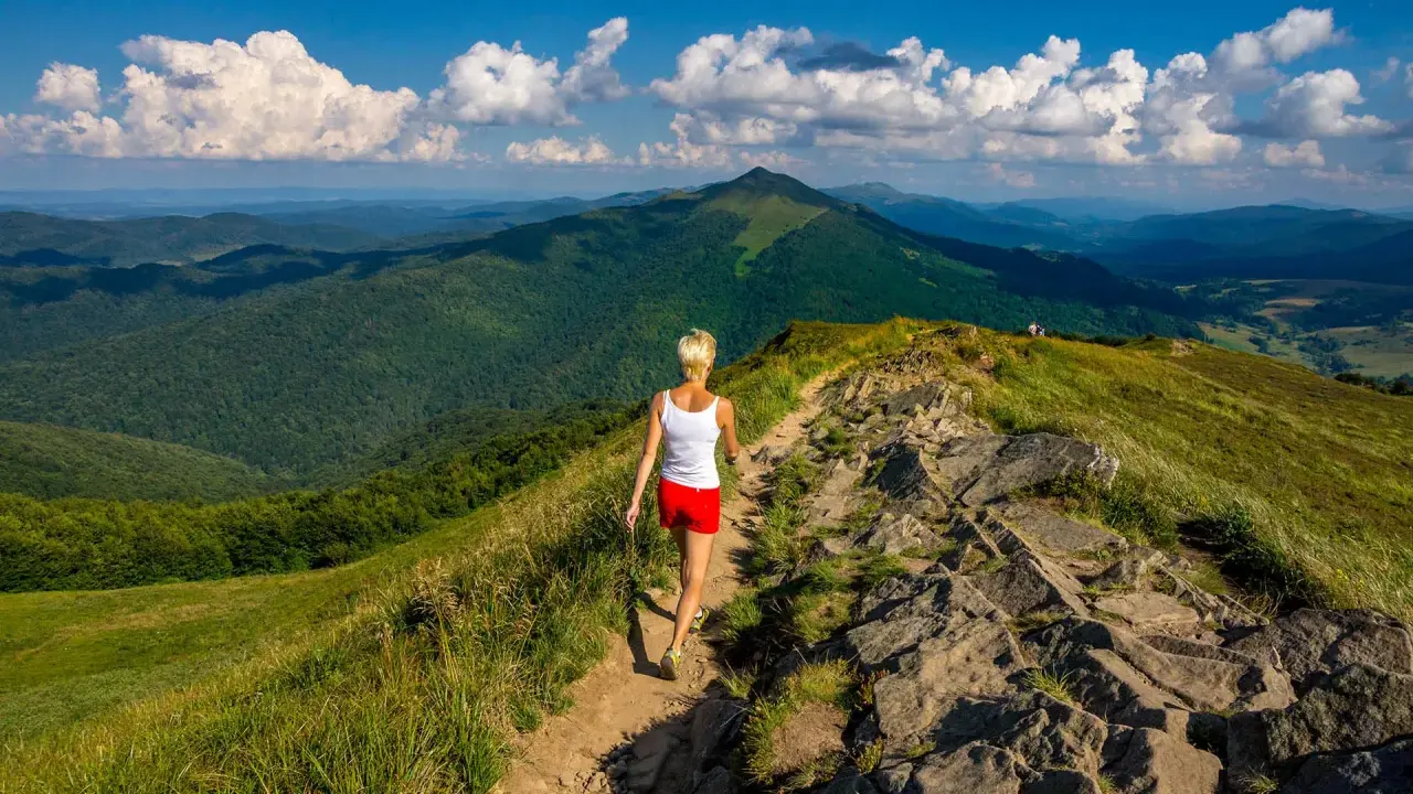 Kobieta wędruje szlakiem pośród zielonych wzgórz. Bieszczady jakie to góry – rozległe, malownicze, z dalekimi horyzontami.