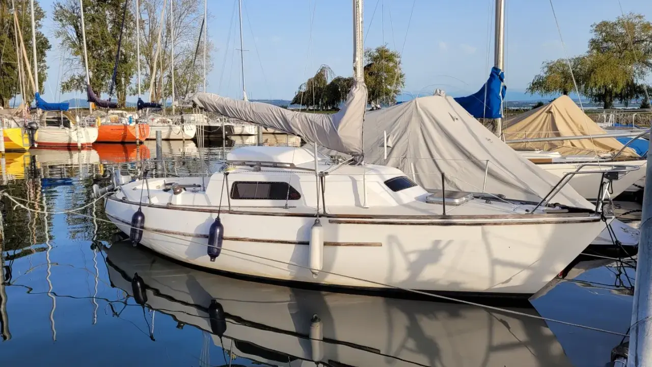 Un voilier blanc, prêt pour l'aventure, est amarré dans un port paisible. Le reflet du voilier sauvignon sur l'eau calme est saisissant.