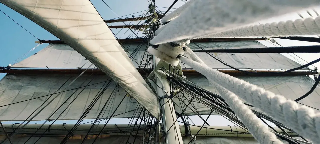 Vue en contre-plongée des voiles d'un voilier, avec le gréement dormant complexe et les cordages épais.