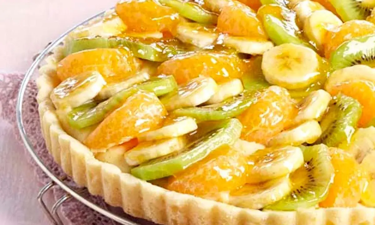 Tarte aux fruits frais sur une base de crème pâtissière. Des rondelles de banane, de kiwi et des quartiers d'orange sont disposés sur le fond de tarte.