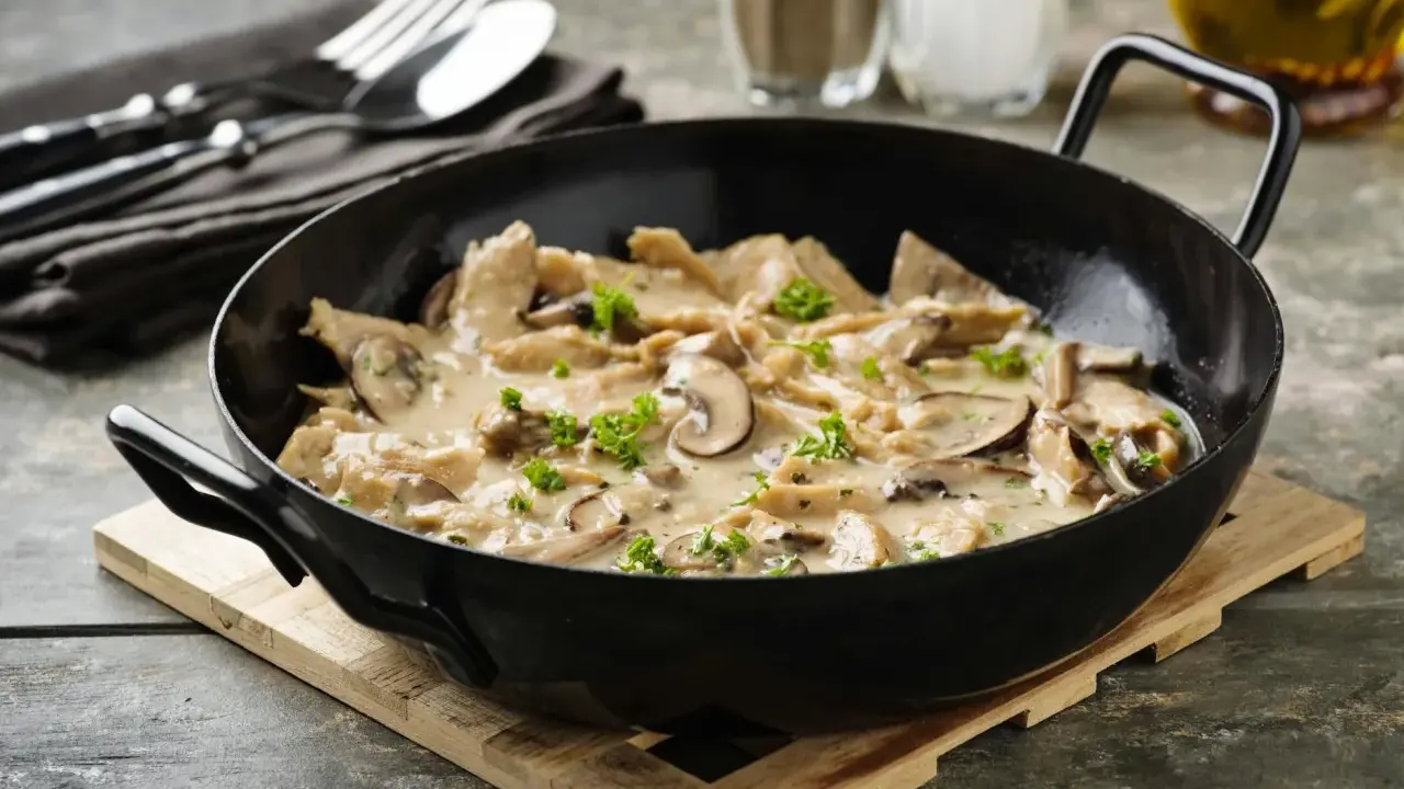 Herzhaftes geschnetzeltes mit Pilzen in cremiger Sauce, garniert mit Petersilie, serviert in einer schwarzen Pfanne.