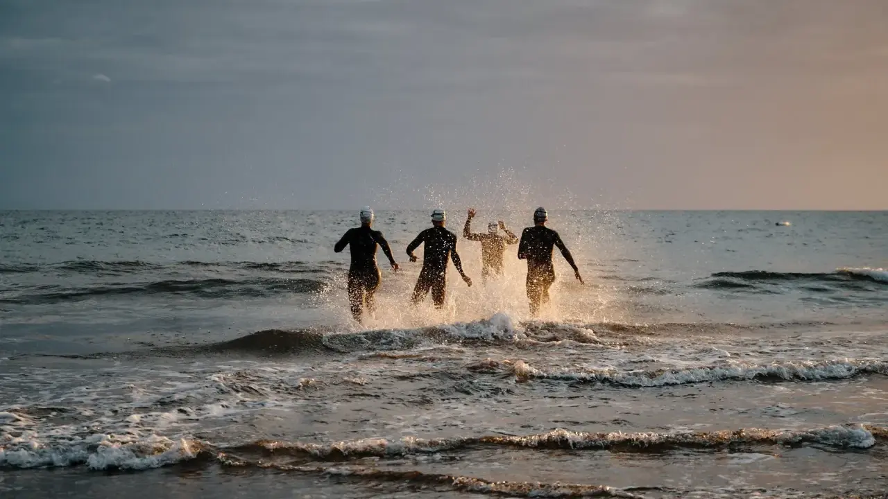 Vier Schwimmer stürmen ins Meer. Die durchschnittliche Zeit für 1km schwimmen wird hier wohl im Wettkampf ermittelt.